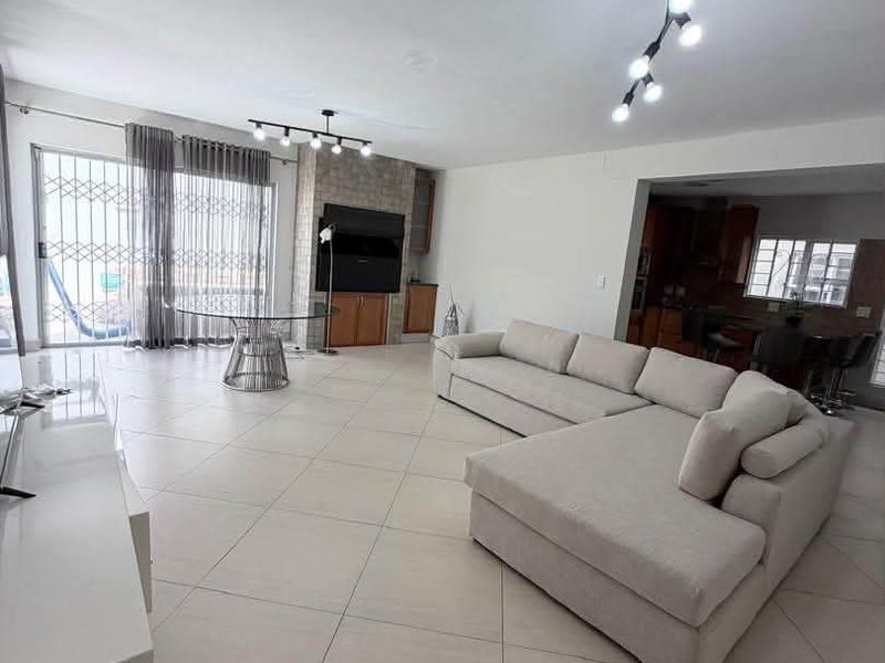 Spacious open-plan living area featuring large format floor tiles, a stone feature wall with built-in shelving, and direct access to the patio.