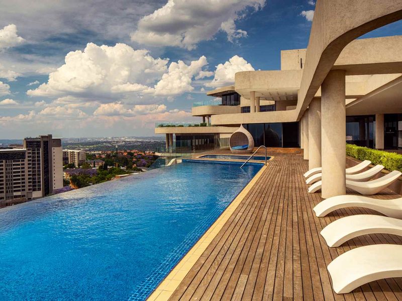 Expansive penthouse terrace featuring a sleek infinity-edge swimming pool, timber decking, and panoramic city views.