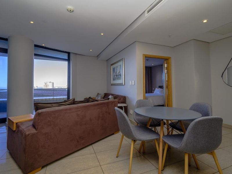 An open-plan living and dining area featuring tiled floors, recessed lighting, and direct access to a balcony through large sliding glass doors.