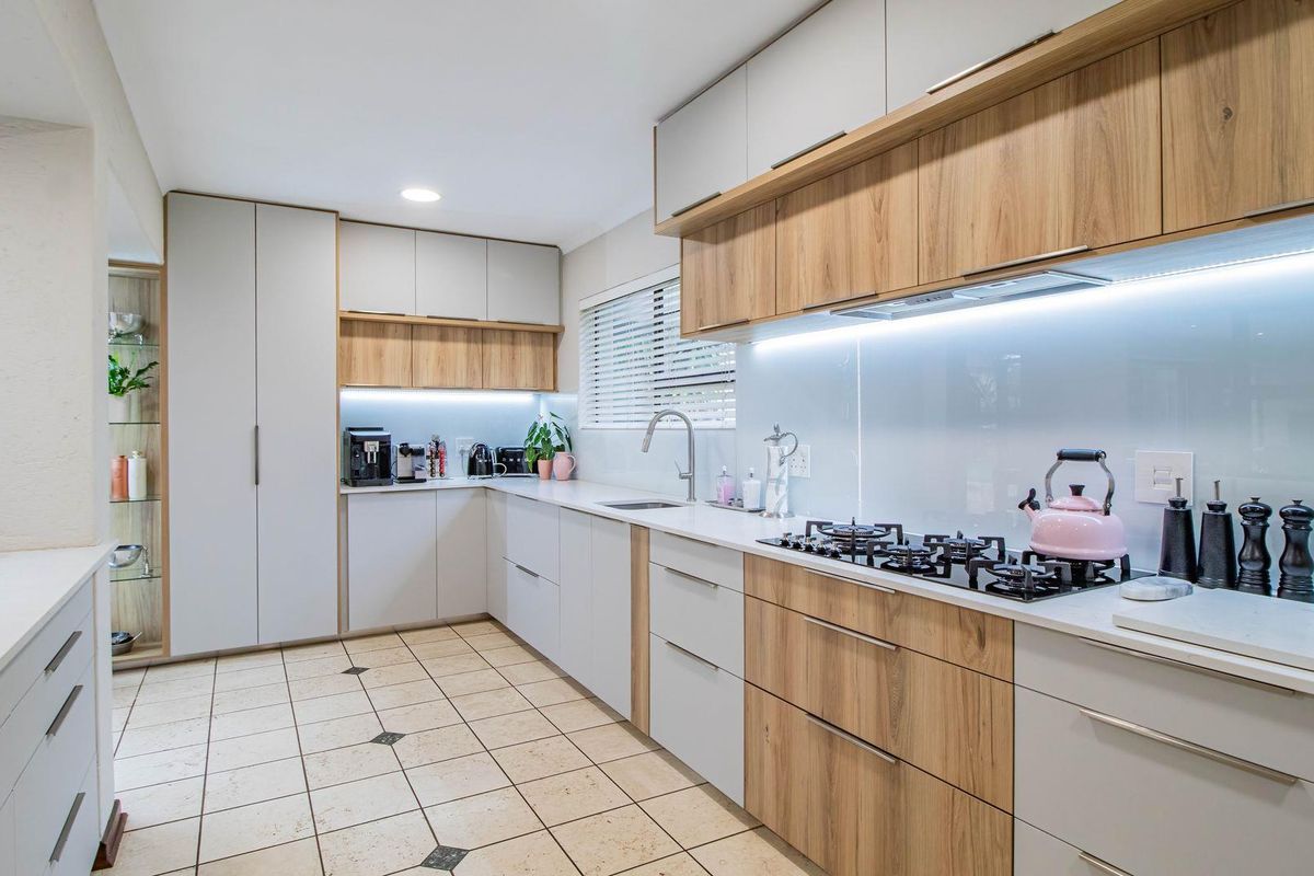 Modern kitchen featuring two-tone cabinetry, stone countertops, integrated gas hob, and under-cabinet LED lighting.