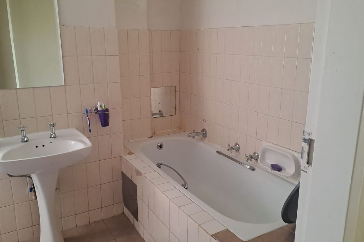 A dated bathroom featuring a pedestal basin and a built-in bathtub with tiled surround, requiring cosmetic updates to modernize the space.