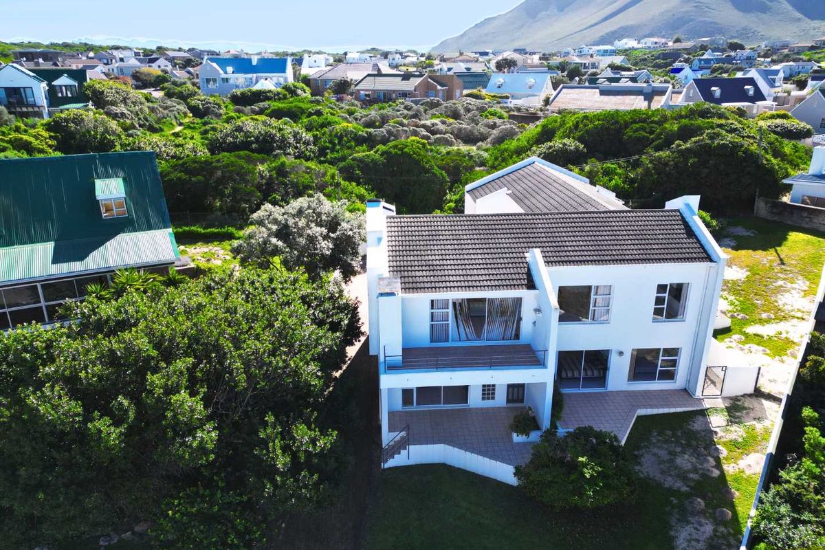 Aerial view of a two-story residential property featuring a tiled roof, balcony, and paved patio area set within a coastal neighborhood.