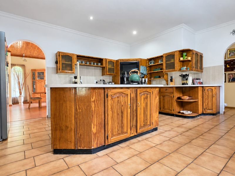 A spacious kitchen featuring traditional wooden cabinetry, tiled flooring, and arched doorways leading to adjacent living areas.