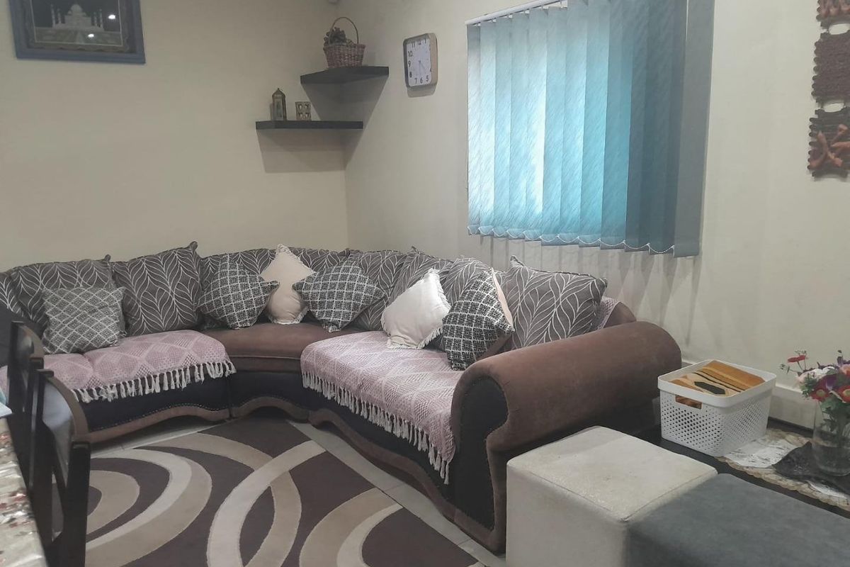 A comfortable living room area featuring tiled flooring, vertical window blinds, and wall-mounted floating shelves.