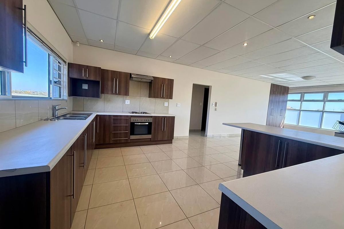 Spacious open-plan kitchen featuring dark wood cabinetry, light countertops, integrated appliances, and tiled flooring, offering a clean and functional layout.