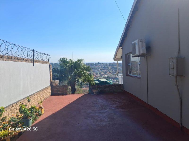 An open-air patio area featuring a brick boundary wall with security razor wire, overlooking a suburban landscape.