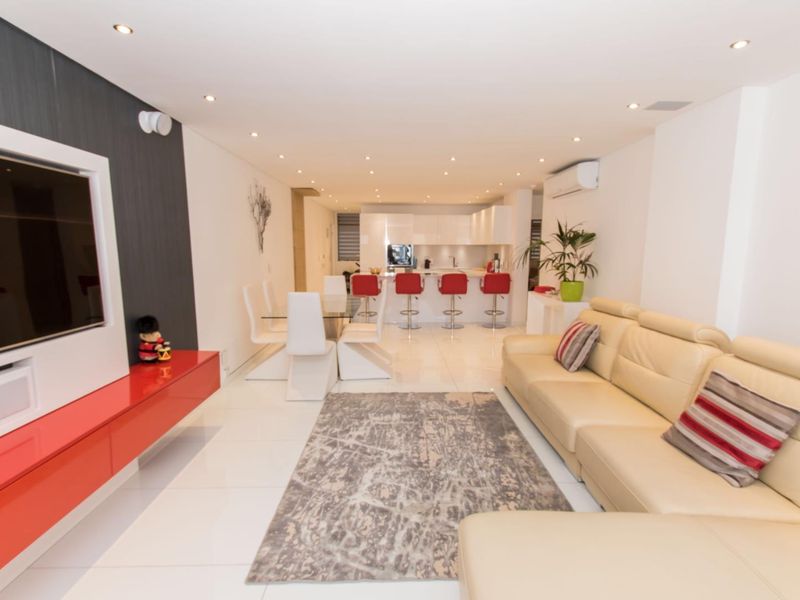 Modern open-plan living and dining area featuring glossy tiled floors, recessed lighting, and a sleek integrated kitchen with a breakfast bar.