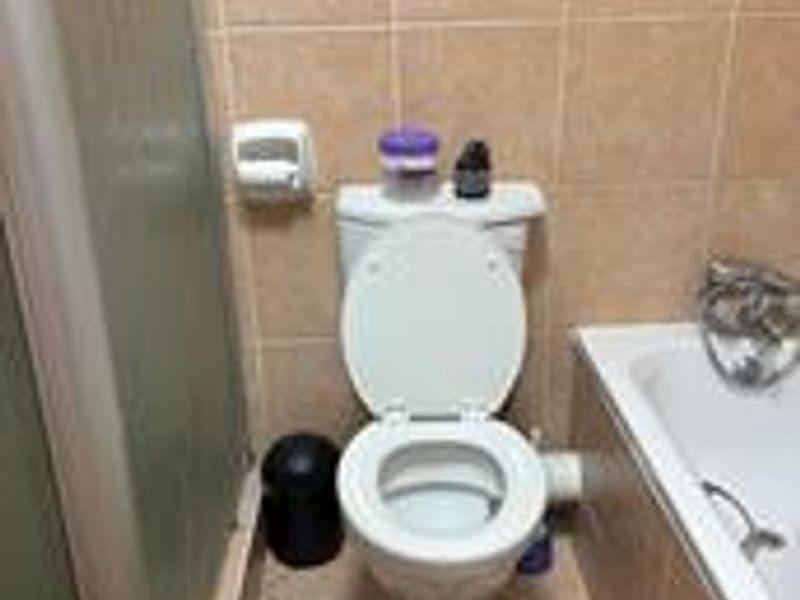 A functional bathroom featuring a standard toilet, bathtub, and shower enclosure with neutral ceramic wall and floor tiling.