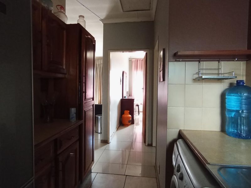 A functional kitchen area featuring wooden cabinetry, tiled splashbacks, and tiled flooring, leading through to an adjacent room.