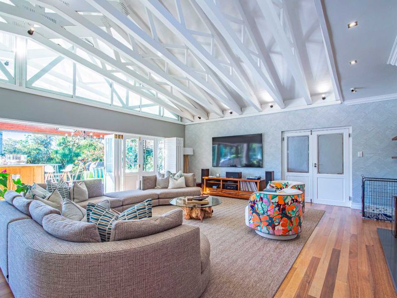 Spacious living room featuring a vaulted ceiling with exposed white timber trusses, hardwood flooring, and large bi-fold doors opening to an outdoor patio area.