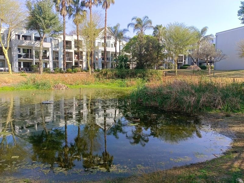 A scenic view of the apartment complex exterior featuring a tranquil pond, landscaped garden areas, and private balconies.