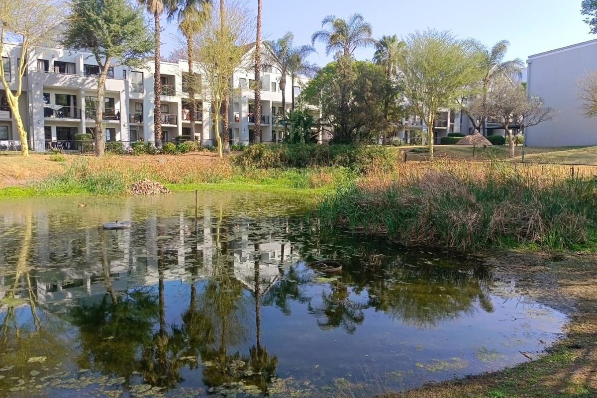 A scenic view of the apartment complex exterior featuring a tranquil pond, landscaped garden areas, and private balconies.