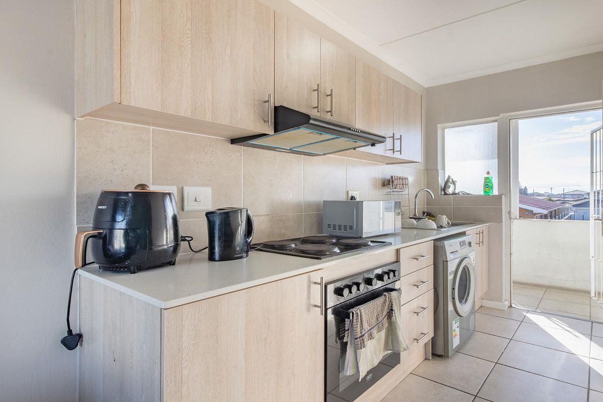 A functional kitchen featuring light wood-finish cabinetry, a built-in oven with electric hob, tiled backsplash, and direct access to an outdoor balcony area.