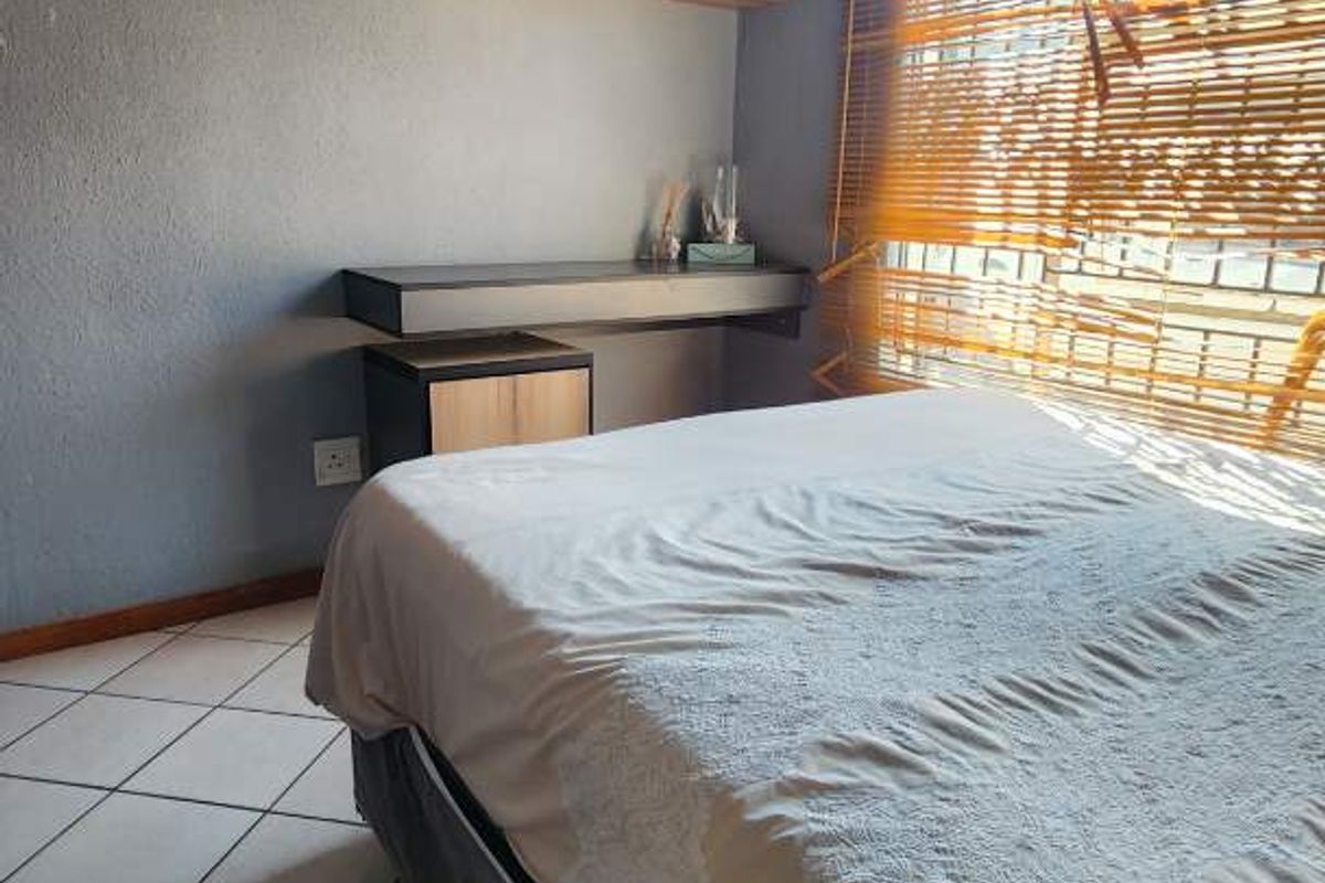 A bedroom featuring tiled flooring, a built-in wall shelf, and a window with fitted blinds.