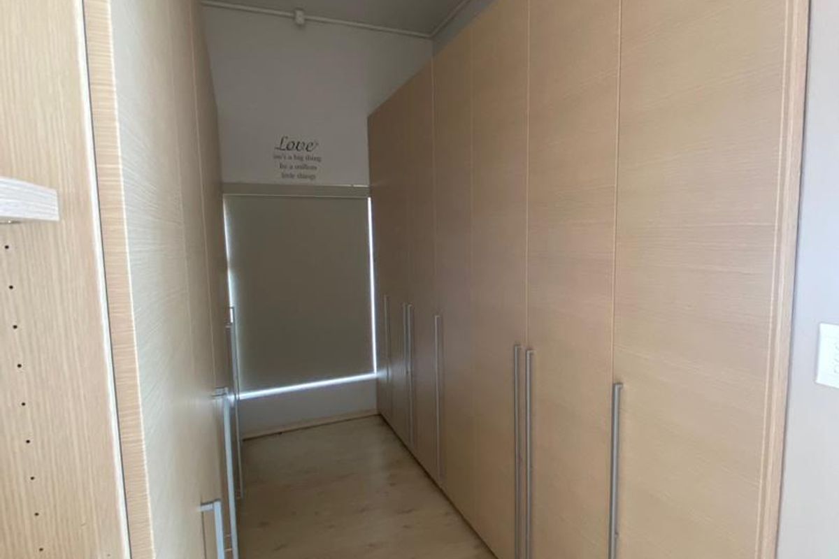 A well-maintained walk-in closet or dressing area featuring extensive built-in light wood cabinetry and laminate flooring.