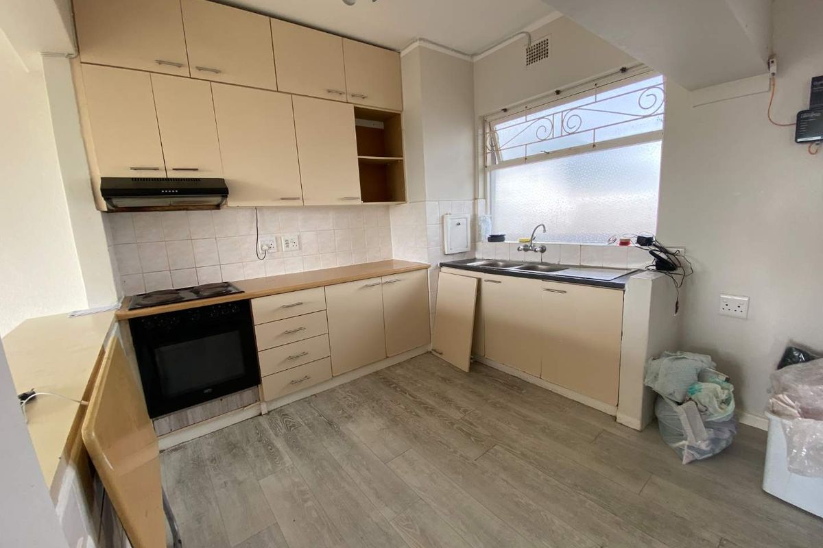 A dated kitchen featuring light-toned cabinetry, a built-in oven and hob, and a double-basin sink with a tiled backsplash.