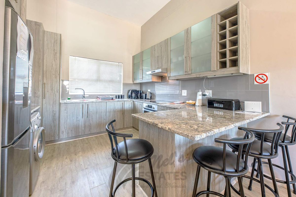 Modern kitchen featuring light wood-grain cabinetry, granite countertops, a breakfast bar, and integrated appliances in a clean, functional layout.