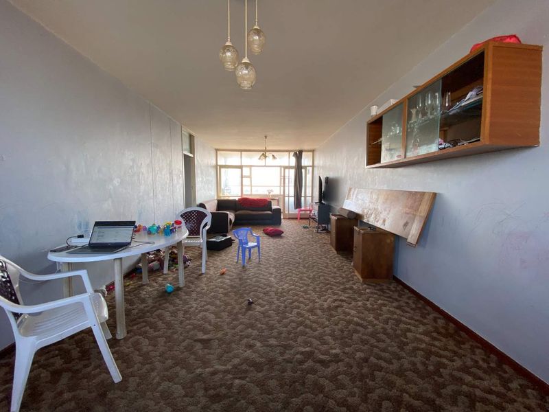 Spacious living area featuring wall-mounted cabinetry, large windows providing natural light, and carpet flooring. The room offers a versatile layout for renovation.