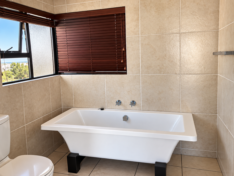 A well-maintained bathroom featuring a modern freestanding bathtub, wall-mounted fixtures, and neutral ceramic tiling throughout.