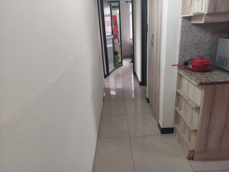 A narrow hallway featuring tiled flooring and built-in cabinetry with granite countertop, showing signs of wear and unfinished base detailing.