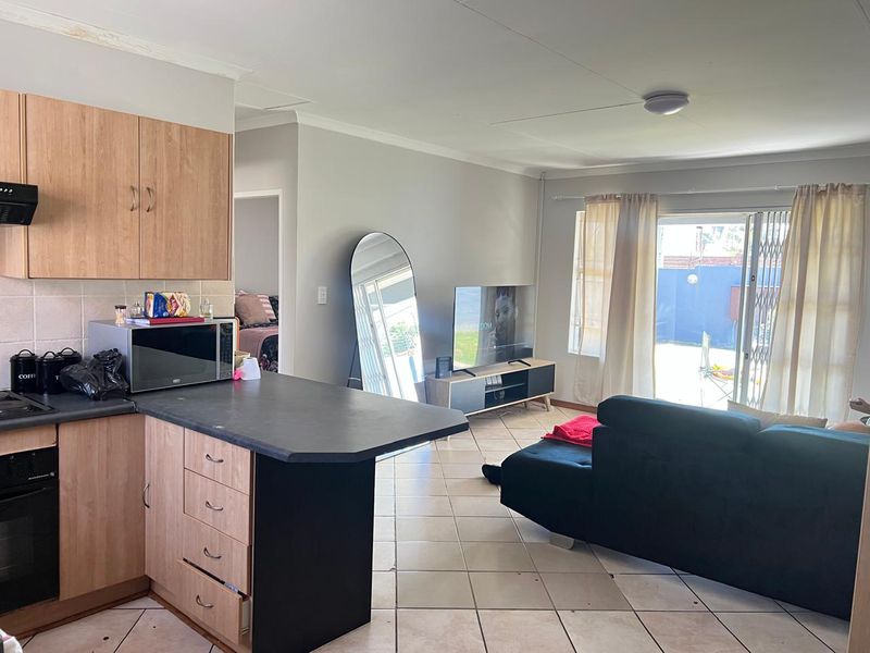 Open-plan living area featuring a functional kitchen with built-in cabinetry and tiled flooring, leading out to a patio through sliding glass doors.
