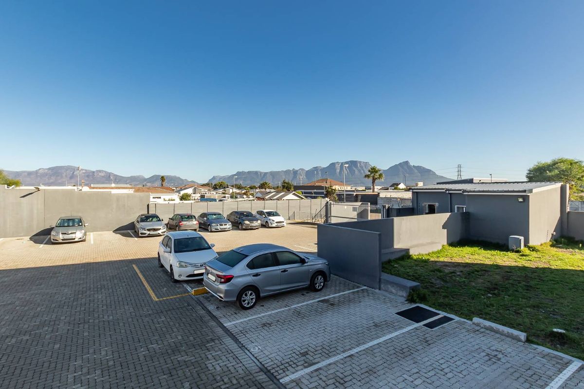An elevated view of the property's rear paved parking area, featuring boundary walls and scenic mountain views in the background.