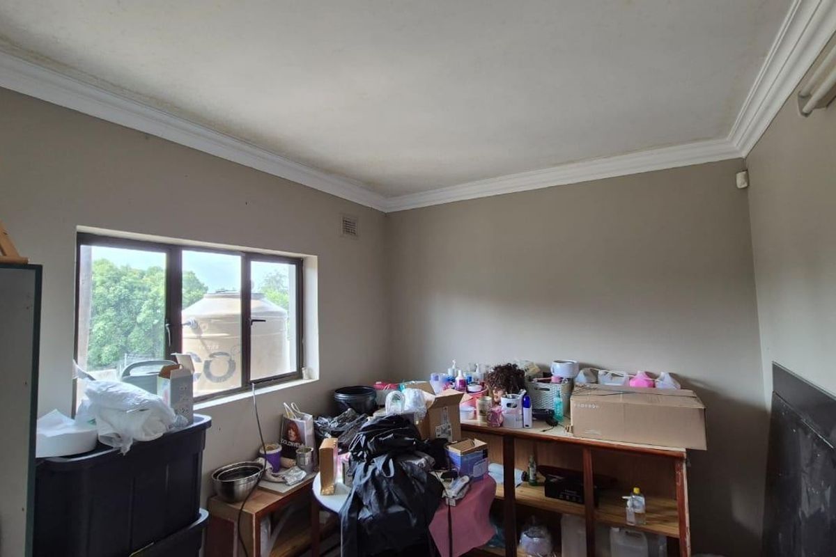 A bedroom space featuring crown molding and aluminium window frames, currently used for storage and in need of cosmetic updates.