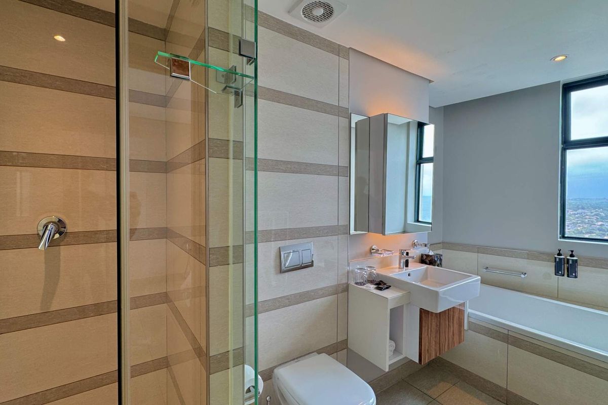 Modern bathroom featuring a glass-enclosed shower, wall-mounted vanity with basin, bathtub, and large window with scenic views.