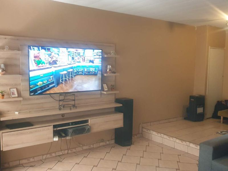 Living room featuring a built-in media unit, tiled flooring, and a raised platform area, offering a functional space for entertainment.