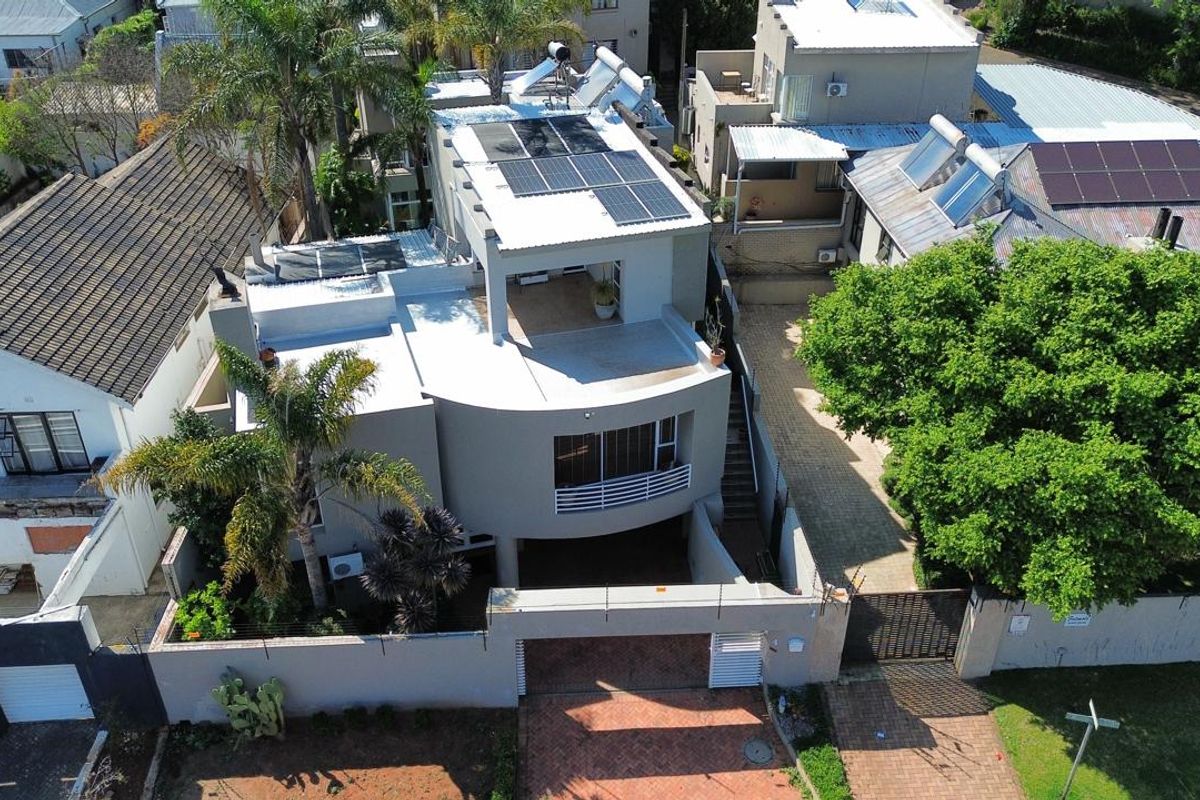 Aerial view of a modern multi-level residential property featuring solar energy installations, a paved driveway, and a secure gated entrance.