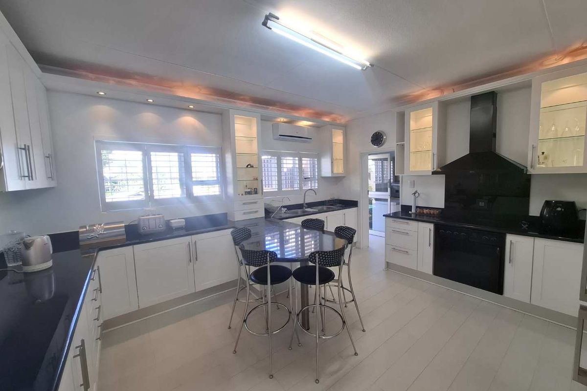 Modern kitchen featuring white cabinetry, dark countertops, integrated oven, extractor fan, and a central breakfast bar area with ample natural light.