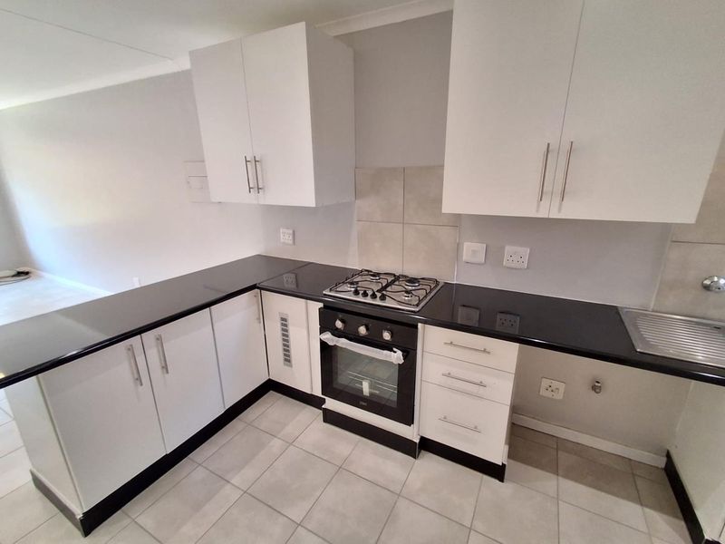 Modern kitchen featuring white cabinetry, black granite countertops, a built-in gas hob, and an oven, with neutral tiled flooring throughout.