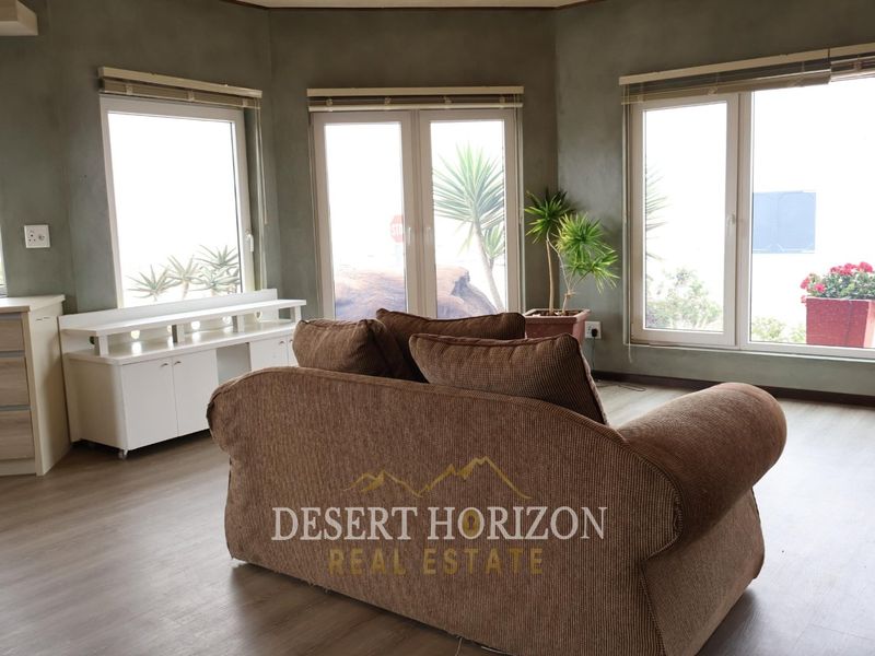 A living room featuring laminate flooring, neutral wall finishes, and multiple windows providing natural light and garden views.