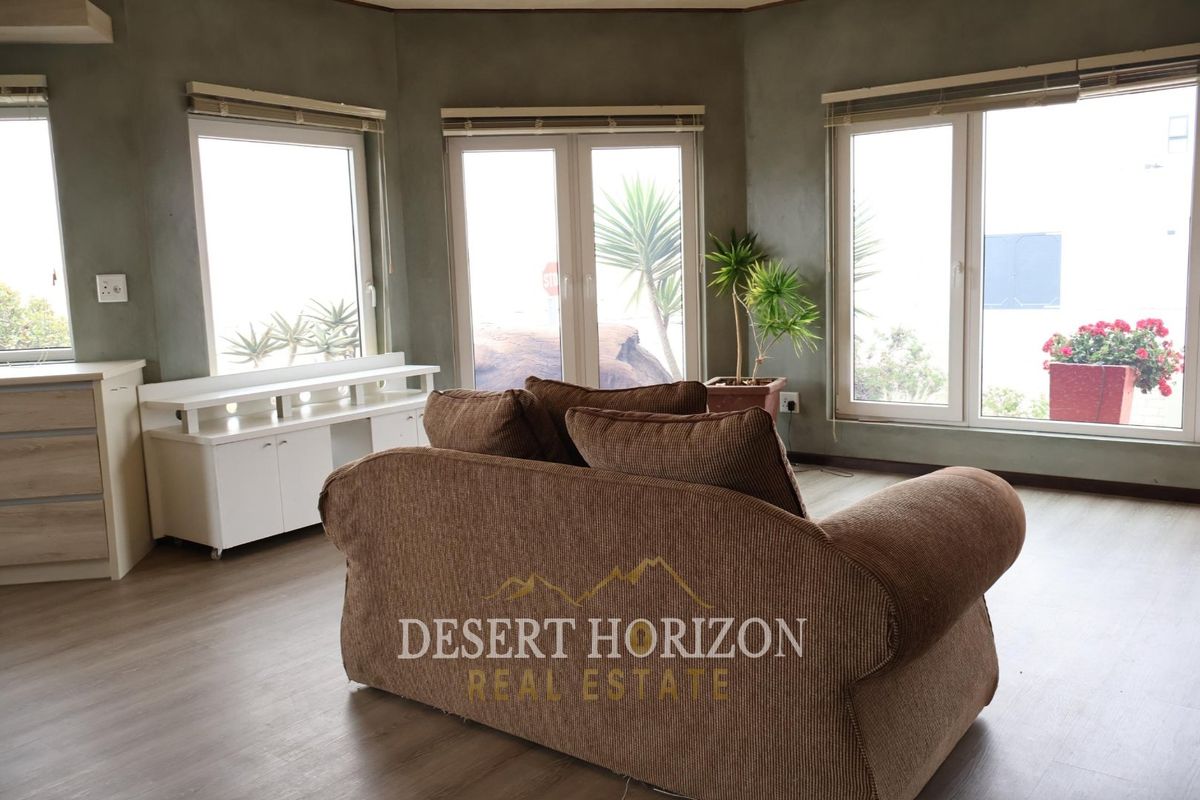 A living room featuring laminate flooring, neutral wall finishes, and multiple windows providing natural light and garden views.