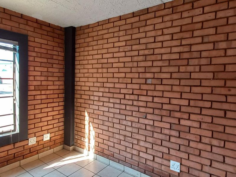An interior office space featuring exposed red brick walls, tiled flooring, and a large window with security bars.