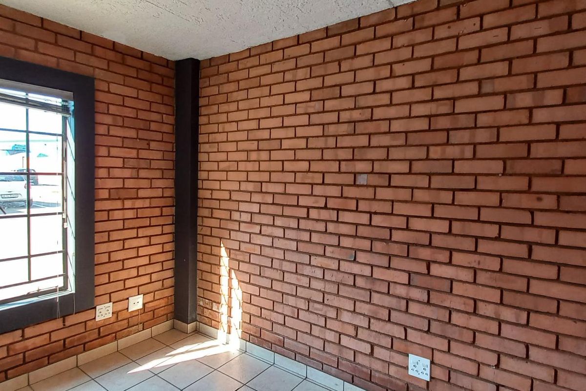 An interior office space featuring exposed red brick walls, tiled flooring, and a large window with security bars.