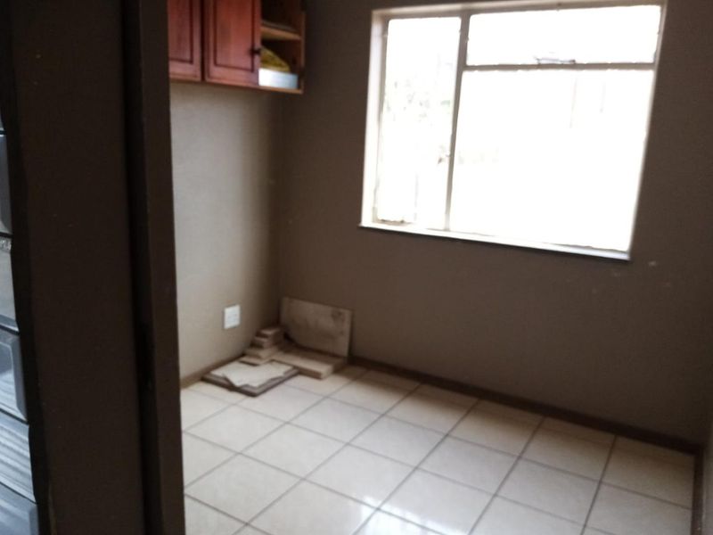 A small, empty utility or laundry room featuring tiled flooring, built-in wall cabinetry, and a large window providing natural light.