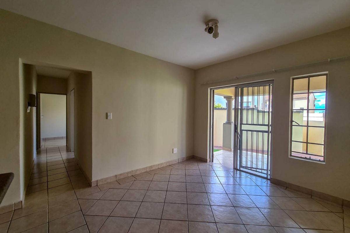 An empty living room featuring ceramic tile flooring, a sliding glass door leading to a patio, and natural light through a window with security bars.