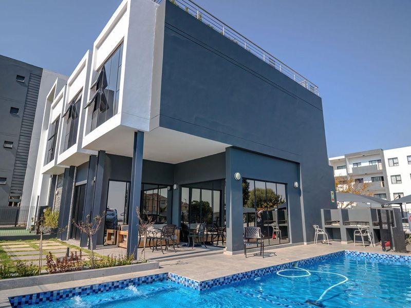Modern apartment complex pool area featuring a tiled patio, built-in braai, and contemporary architectural design with large glass sliding doors.