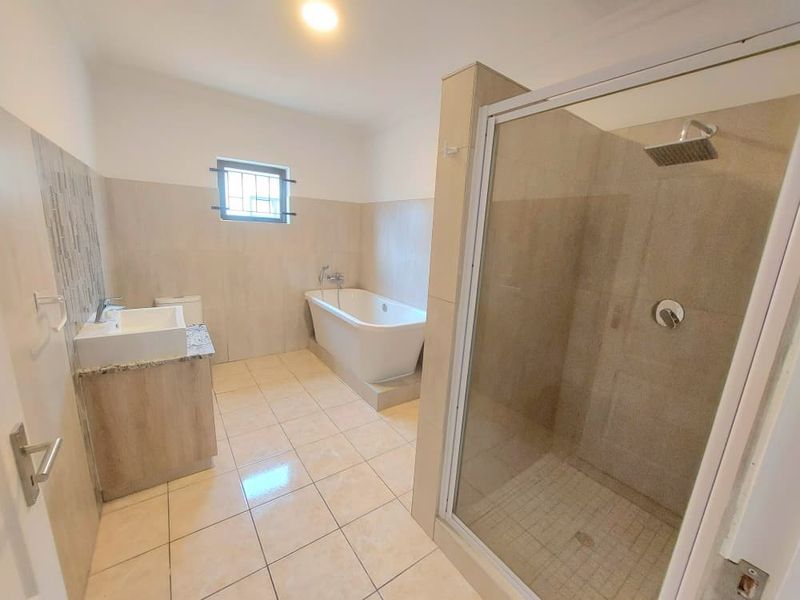 A modern, spacious bathroom featuring a freestanding bathtub, a separate glass-enclosed shower, and a vanity unit with neutral wall and floor tiling.