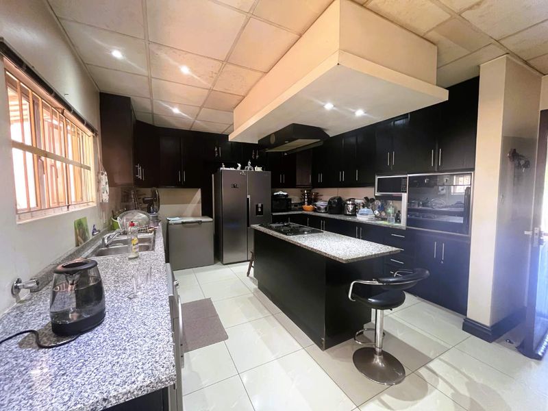 Spacious kitchen featuring dark cabinetry, granite countertops, a central island with a built-in hob, and integrated oven, complemented by tiled flooring.