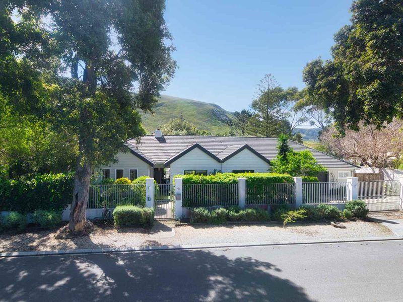 Front elevation of a single-story house featuring a tiled roof, secure metal perimeter fencing, and gated access, set against a scenic mountain backdrop.