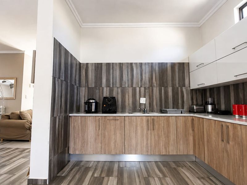 Modern kitchen featuring wood-look cabinetry, contrasting tiled backsplash, and laminate flooring, seamlessly flowing into the adjacent living area.