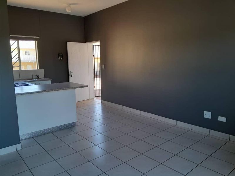 An open-plan living and kitchen area featuring tiled flooring, a breakfast bar, and direct access to an exterior security gate.