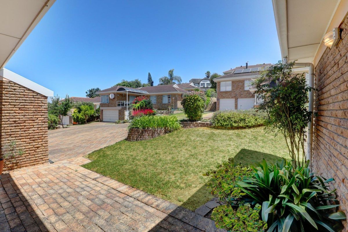 View of the communal garden area and paved driveway from a covered patio, showcasing the townhouse complex exterior and landscaped surroundings.