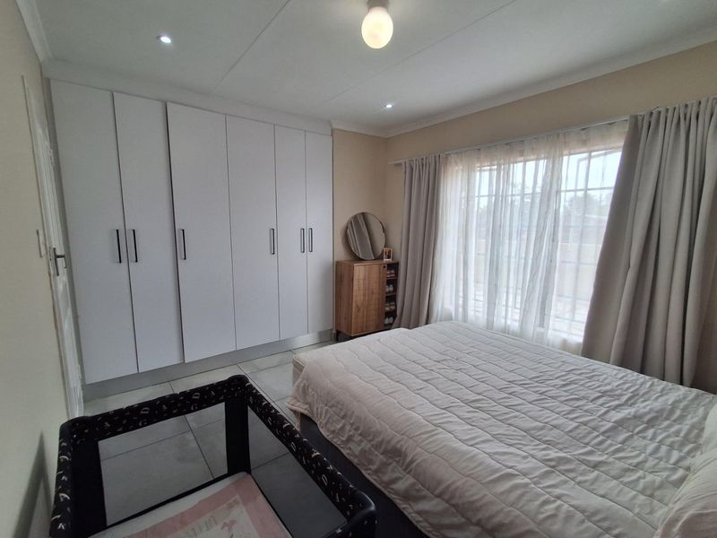 A well-maintained bedroom featuring built-in cupboards, tiled flooring, and large windows with security bars, providing a functional and comfortable living space.