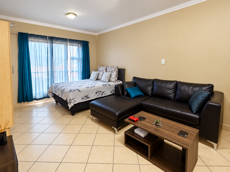 An open-plan living and sleeping area featuring neutral wall tones, ceramic floor tiles, and a large sliding glass door providing natural light.