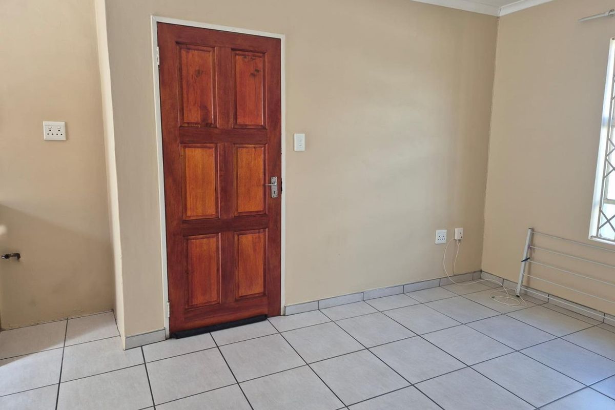 A simple interior room featuring tiled flooring, a solid wood panel door, and a window with security bars.