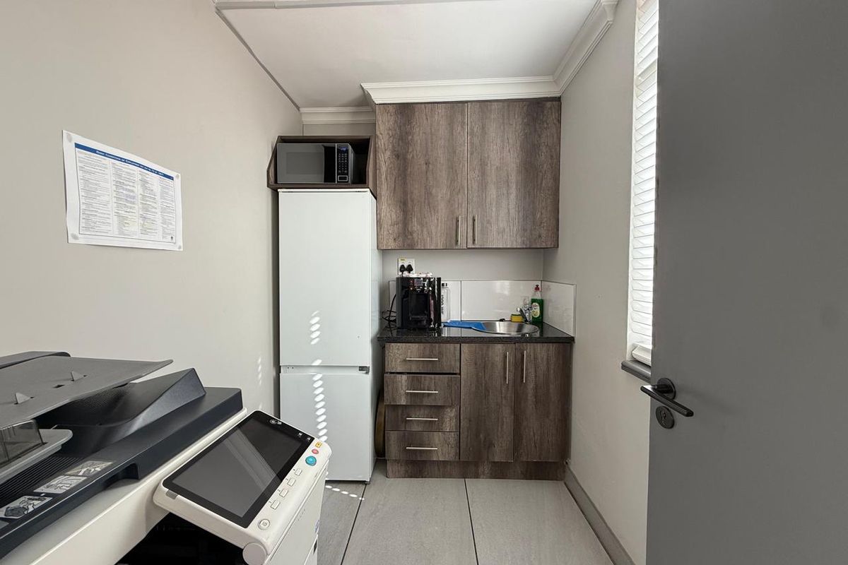 A compact office kitchenette featuring wood-look cabinetry, a small sink, and tiled flooring, designed for efficient workspace utility.
