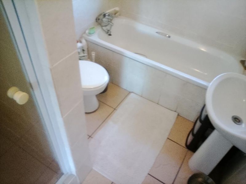 A functional bathroom featuring a standard bathtub, pedestal basin, and toilet with neutral tiled finishes throughout.